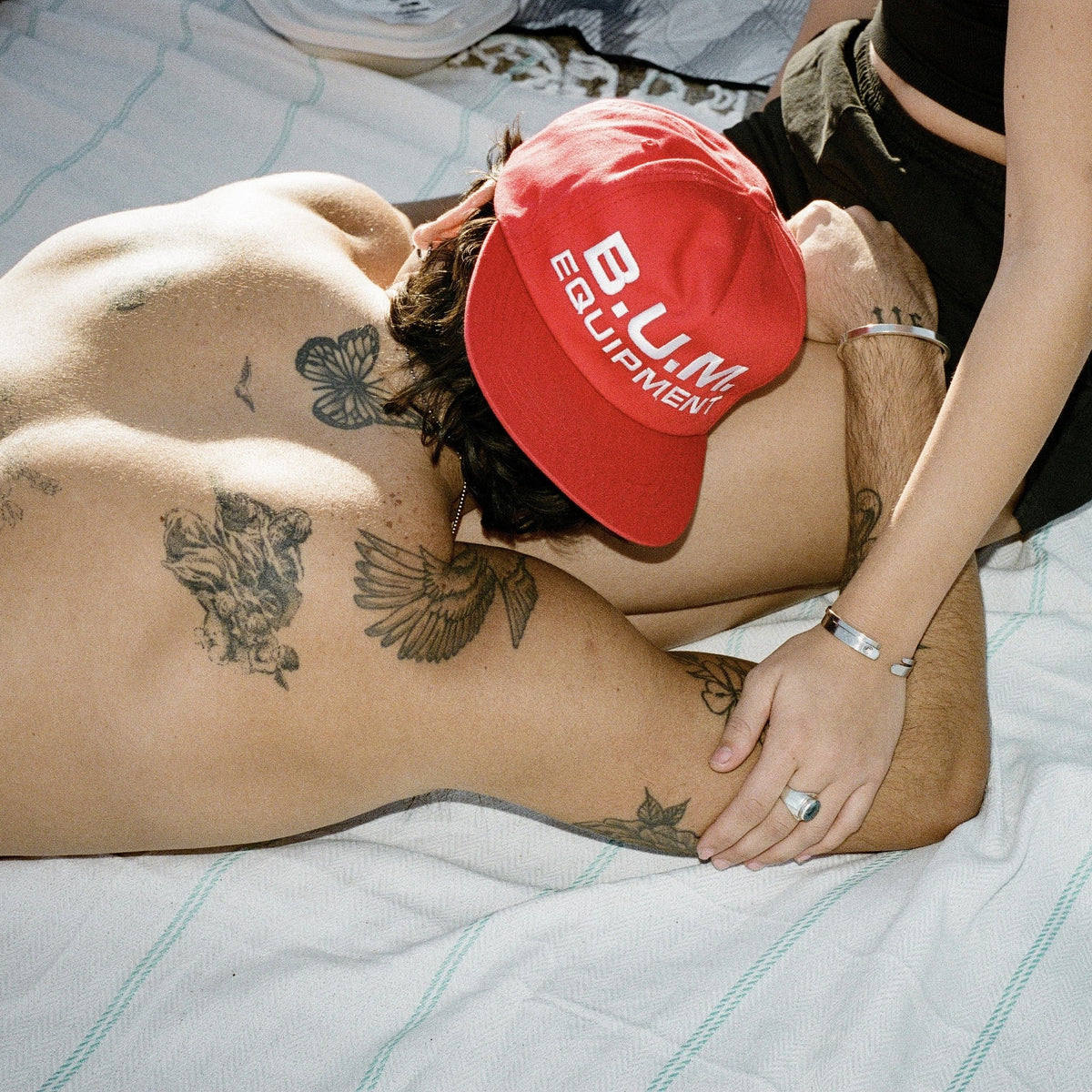 Man lying on a blanket with the red B.U.M. Equipment snapback cap over his face