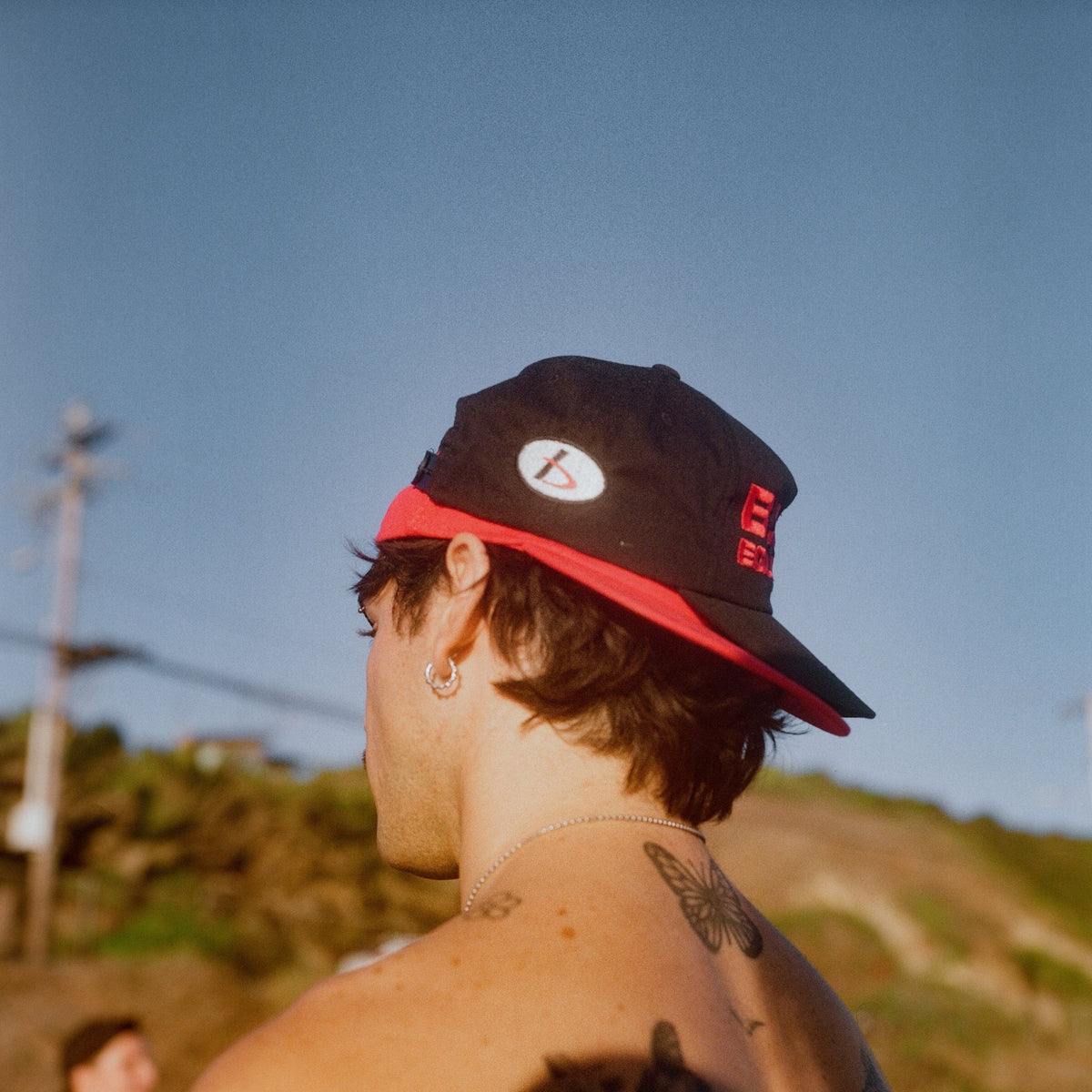 Man photographed from behind at golden hour wearing the B.U.M. Equipment black snapback cap with a red under brim