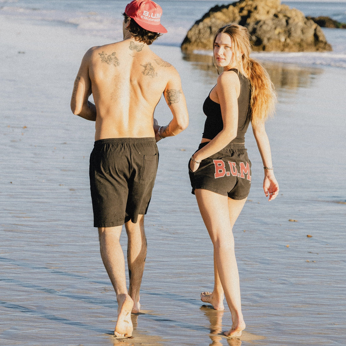 Woman walking at the shoreline in the B.U.M. Womens Shorts in black with the arched B.U.M. logo on the back